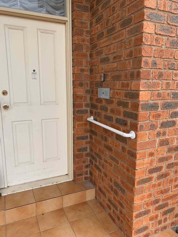 Stainless steel grab rail installed on brick beside a front door step