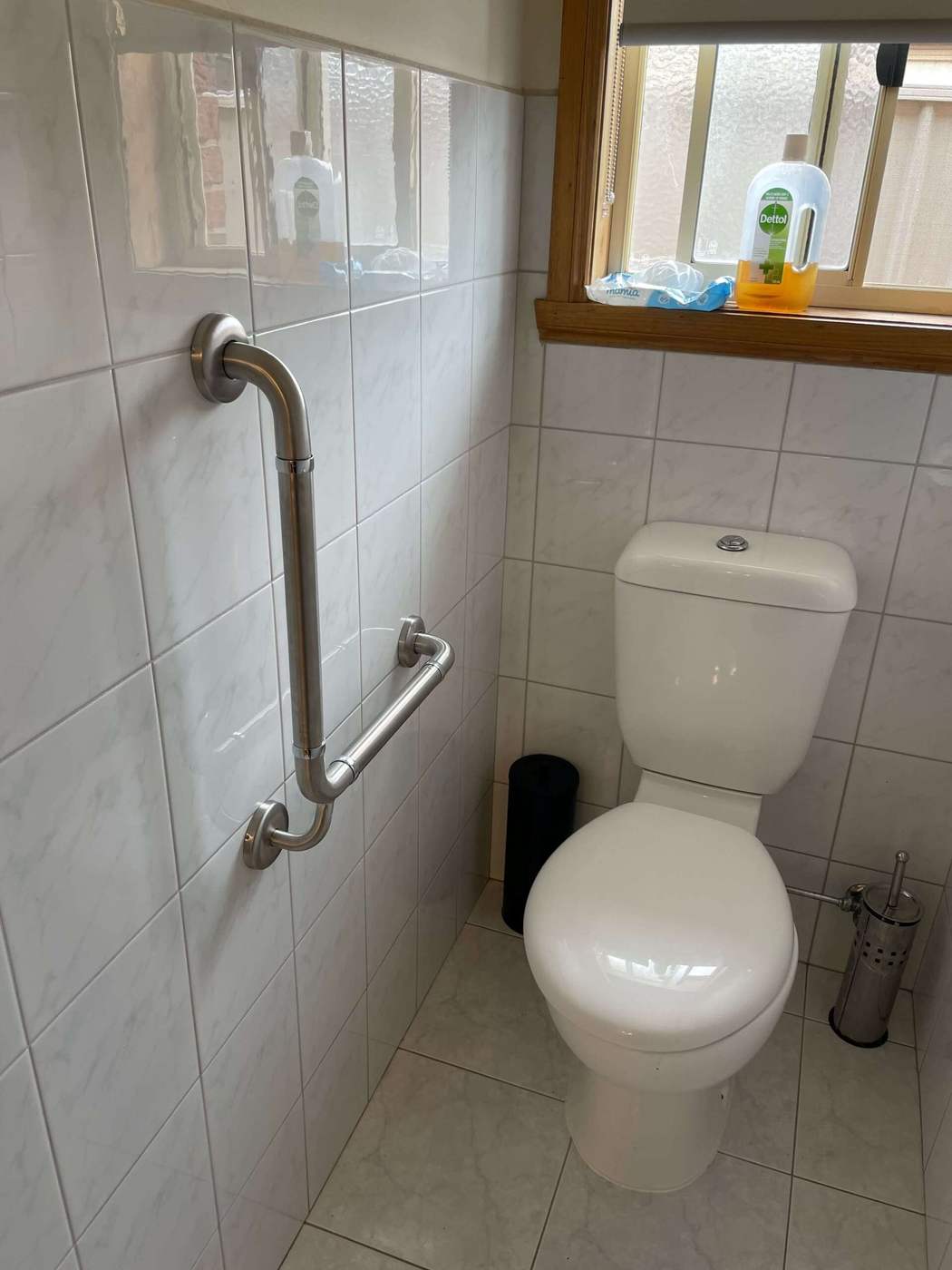 Stainless steel grab rail installed beside a toilet on tiled wall