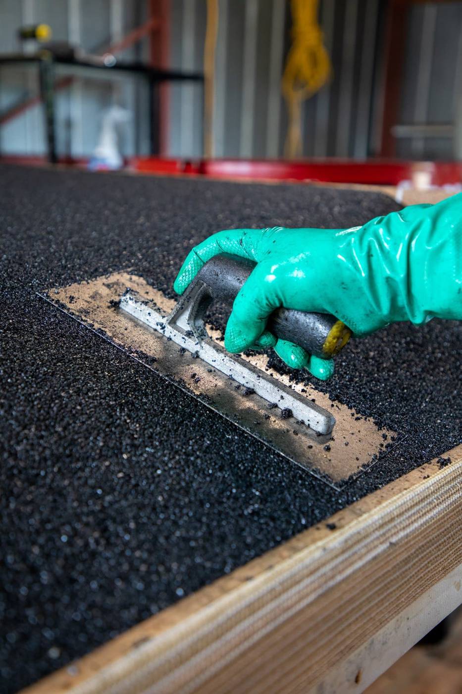 Gloved hand trowelling the bonded rubber surface of a new ramp