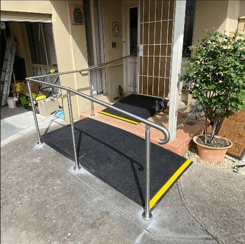 Rubber wheelchair ramp with stainless steel handrails and yellow nosing at a front step
